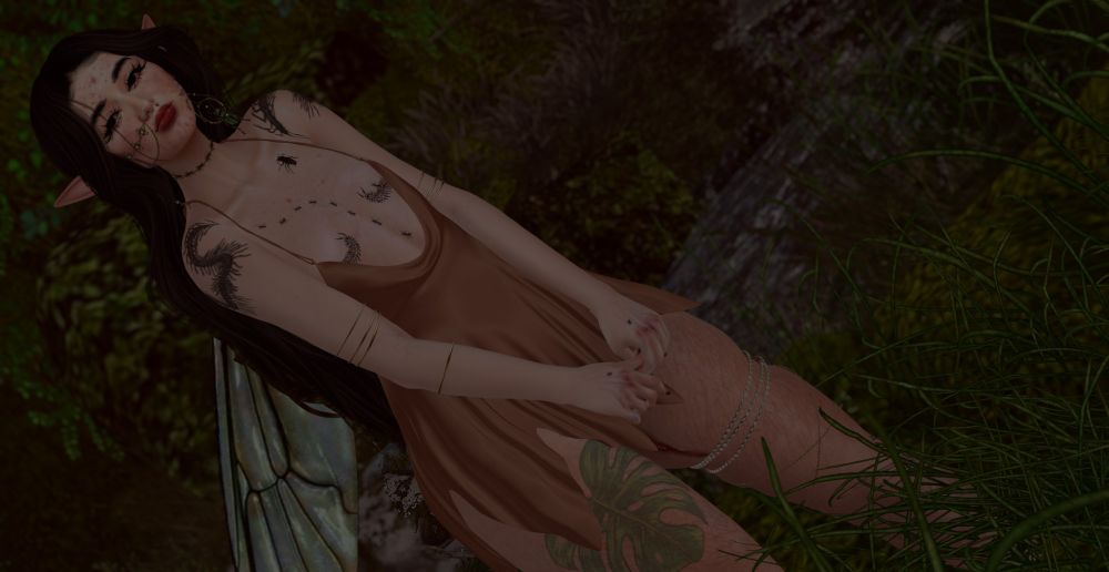 Secondlife Avatar Persona Faerie, she's in a brown/tan dress with long black hair and bug tattoos. she's in a forest setting and she's honestly darn cute. 