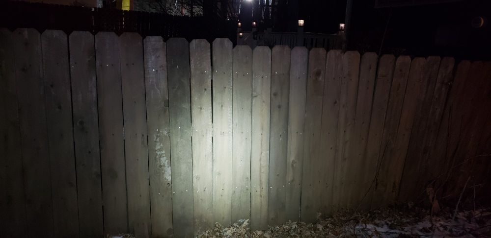 A photo of an old wooden fence taken at night. A number of shiny new screws glint in the light from the flash.
There is ice and snow on the fallen leaves on the ground.