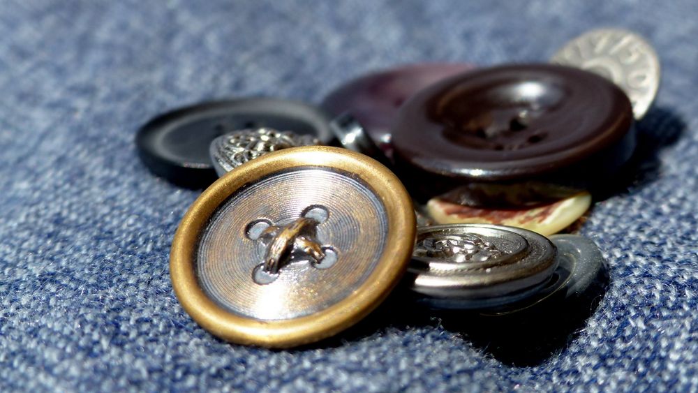 Ein kleines Sammelsurium an Knöpfen in Großaufnahme auf blauem Stoff