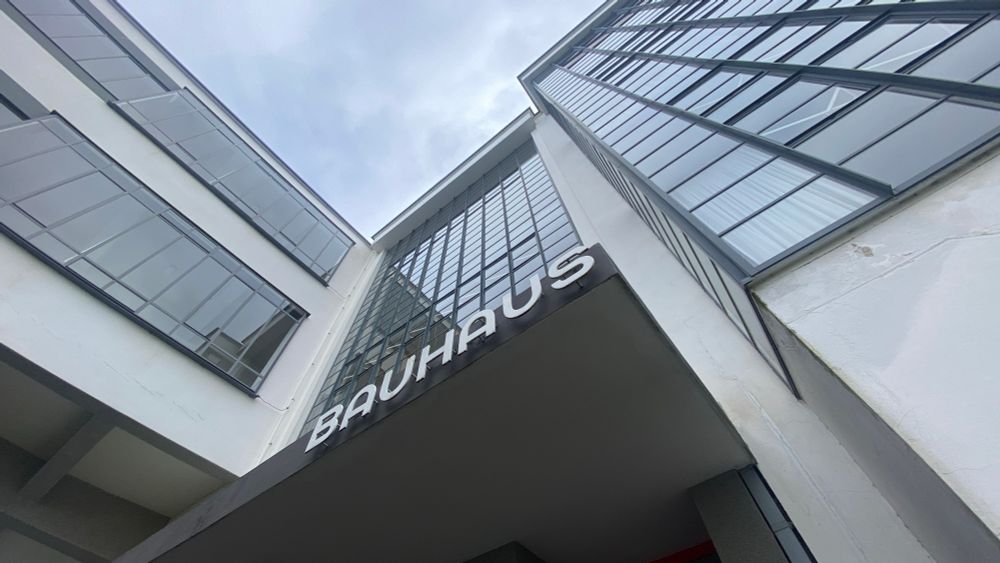 Der Eingang des Bauhaus-Gebäudes mit seiner rechtwinklig verglasten Fassade vor grauem Himmel. Schräg von unten mit stürzenden Linien fotografiert 