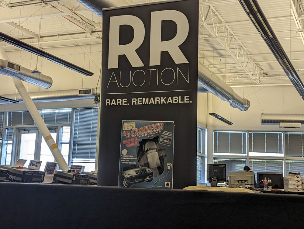 RR Auction booth with a big poster. The table is empty except for a boxed PT Cruiser mouse.