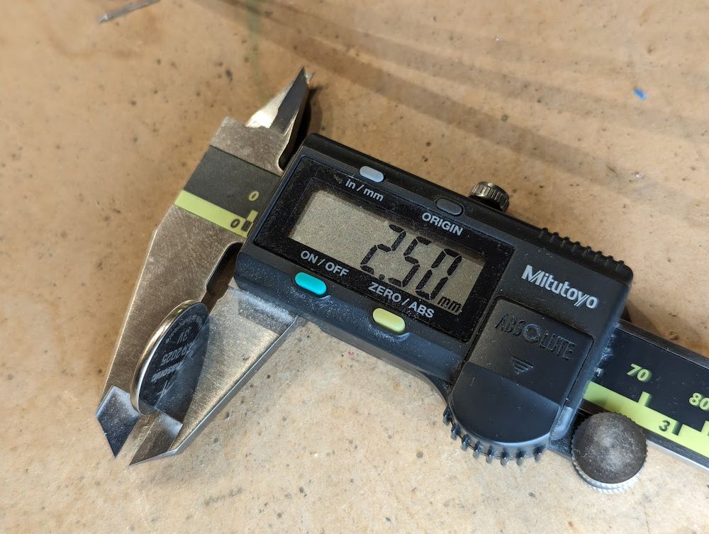 a digital caliper measuring the thickness of a coin cell (2.5mm) but the caliper is made of metal, obviously shorting out the coin cell.