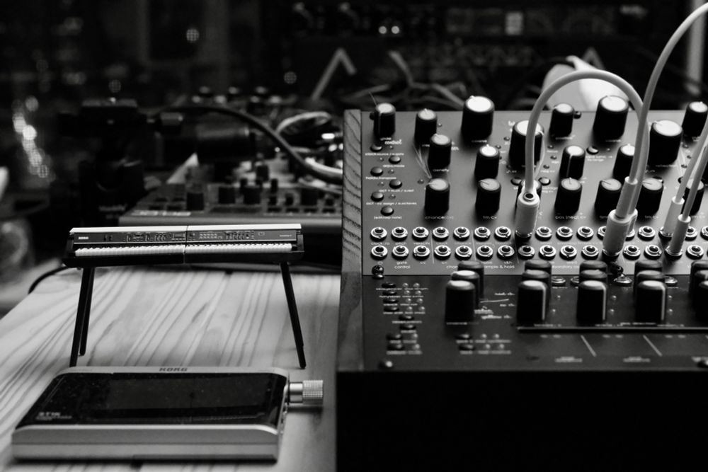 Night photo of half of a modular synthesizer next to a toy Korg e-piano and Korg synth tuner
