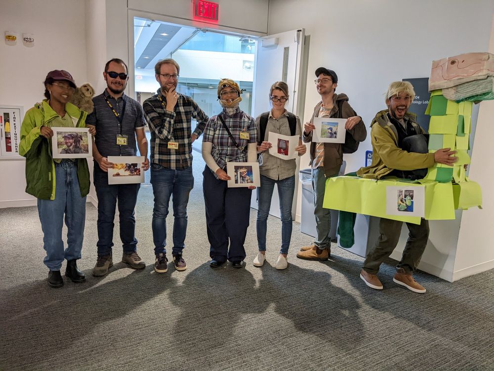 Several people in a corridor. Matt is in the center, flanked by grad students dressed as Matt, wearing the same outfits as Matt is shown wearing in pictures they are holding.