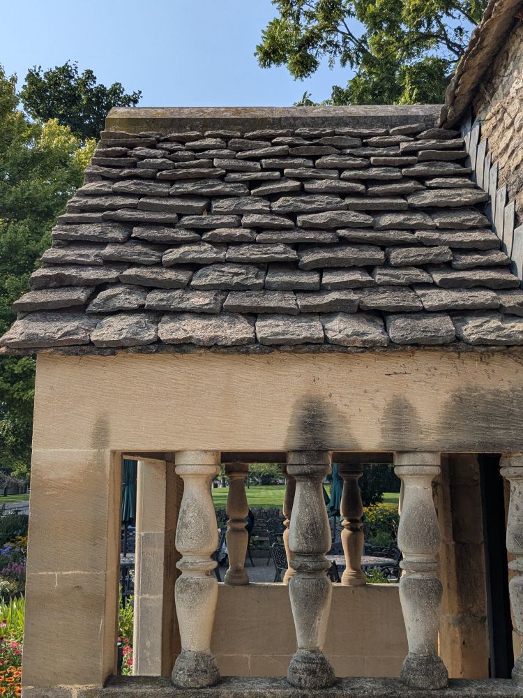 Gray stone roofing slates seen above a cottage entry clad in honey colored Cotswold stone.
