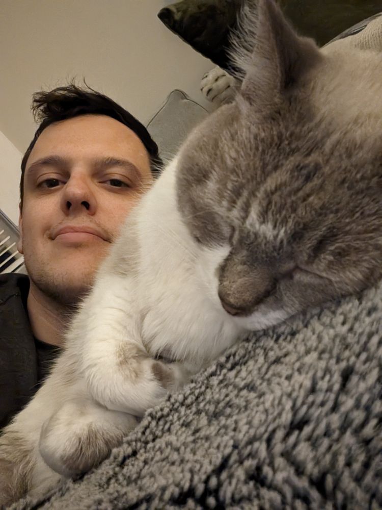 A sleeping gray and white cat called Pavas in the foreground with a sleepy looking Phil behind her