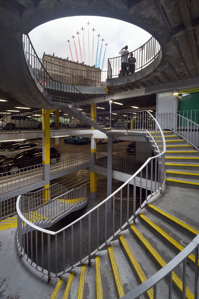 A spiral staircase in a lovely concrete carpark. Out the top  of the stair you can see the sky, Edinburgh Castle, and the Red Arrows.