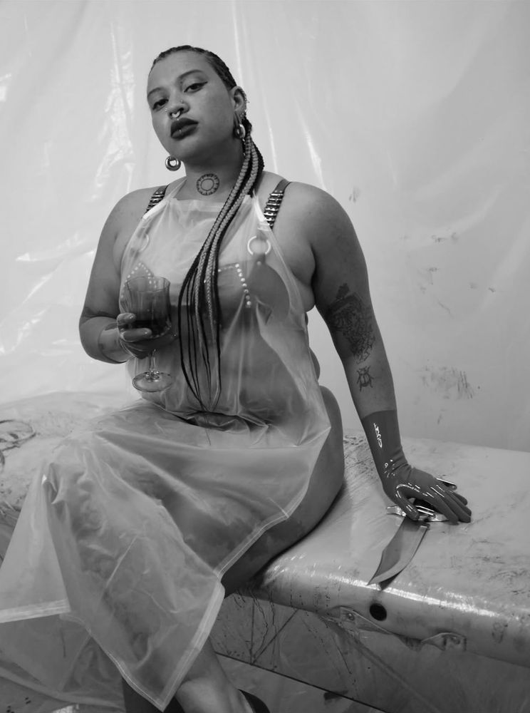 Tomi sits on a plastic wrapped massage table. Tomis latex gloved hand rests on a huge hunting knife. 