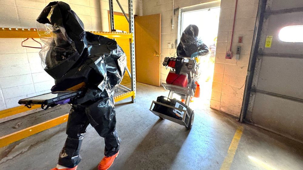 Two National Guard members wearing protective suits enter a building on the UNMC campus during the drill