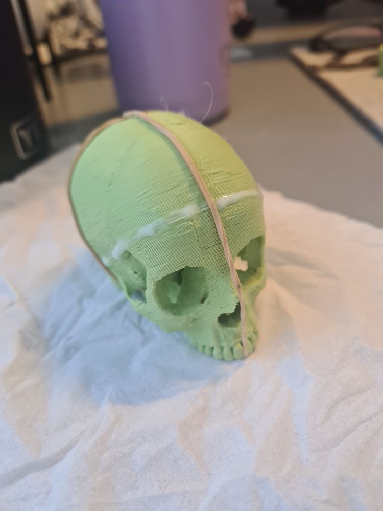 A 3d printed, jawless, green skull, the size of a large kiwi fruit (you're so welcome). It has elastic bands going around front to back and left to right, holding it in place as the top of the top of the head is being glued to the bottom 