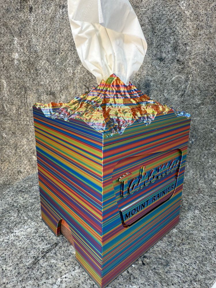 To Home a tissue box cover that is 3-D printed with the tissue coming out of the top that changes colors very very quickly from layer to layer to make it look like rainbowINSAR. There is a script “Tahoma“ with Mount Rainier underneath in the style of Forest service signs.