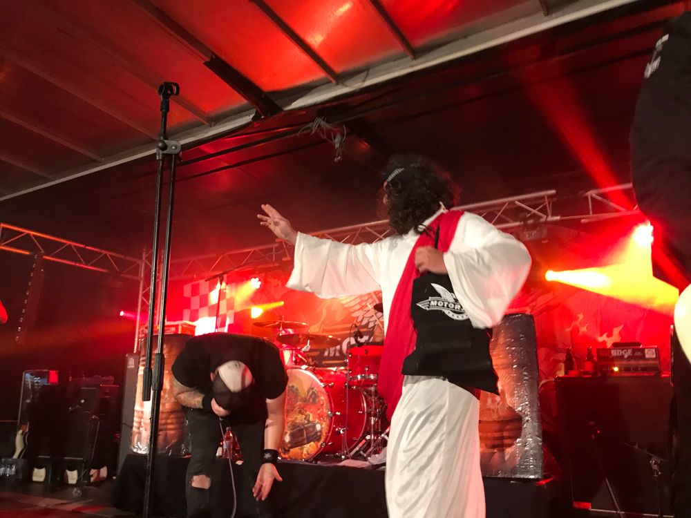 Ein Mann als Jesus verkleidet, verteilt auf einem Motorjesus Konzert Bier