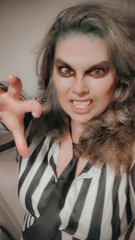 Actress model Tamara Kane dressed as Beetlejuice, black and white striped shirt, black satin tie, big teased up hair, growly wild fierce face, hand making a claw gesture.