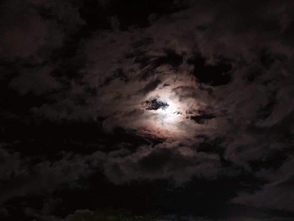 A slightly edited picture of a full moon, surrounded by clouds.