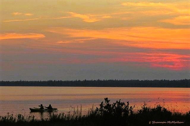 A sunset of mauves, pinks, purples and orange reflected in Lake Huron while kayakers are silhouetted in the foreground.                  