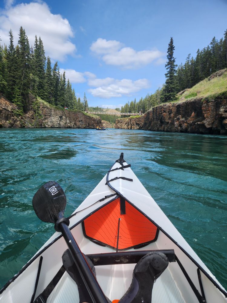 The view from my kayak as I drifted down the vibrant blue-green waters of the Whitehorse River, flanked on either side by rocky cliffs