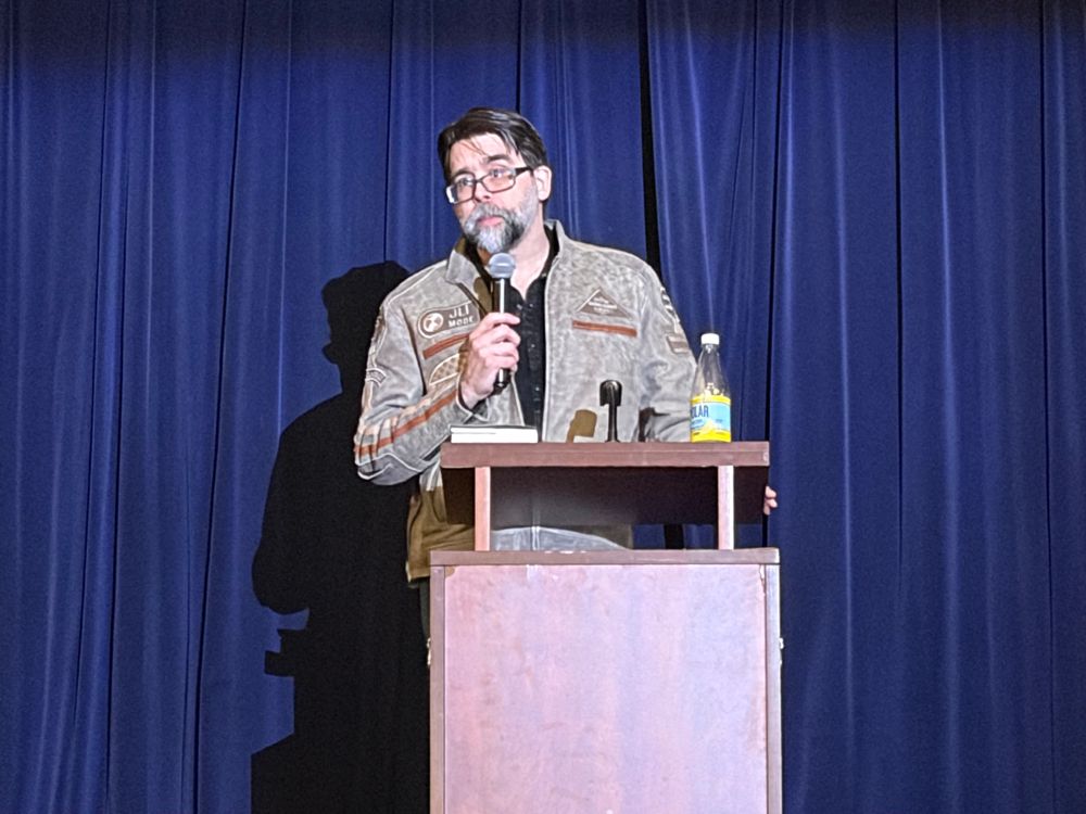 Joe Hill with a microphone on stage at a book launch.