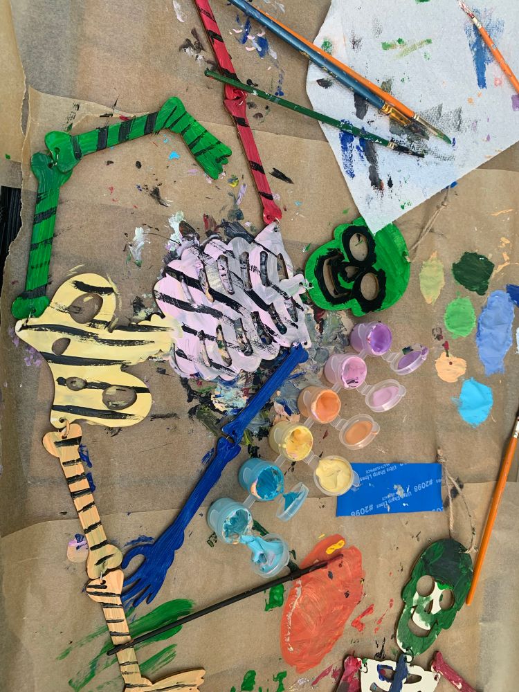 A messy hand painted wooden skeleton on craft paper with paintbrushes