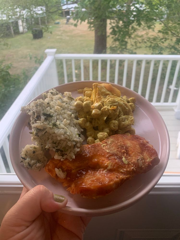 BBQ chicken, dill/parsley rice and curry/garlic/ginger sour cream chickpeas on a plate in front of an outdoor porch.
