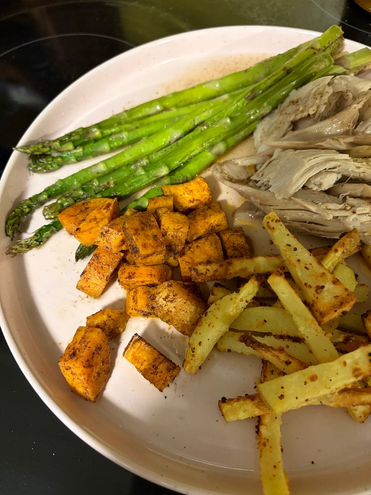 Aparagus, jerk turkey, sweet potatoes, and potato frites on a plate 