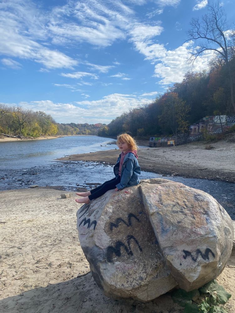Child sitting on a big rock overlooking where creek and river merge
