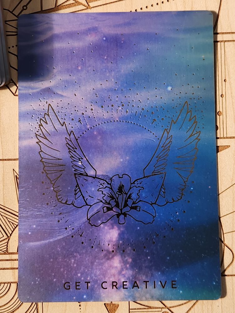 card text reads: "get creative." the background is of the water's surface, with small ripples or waves. the main design is of an iris blossom. two crystals sit just behind it. from there, a pair of wings spread out. many small sparks surround the design in a circle.