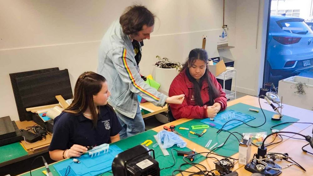 Two young girls working with a young man on a soldering project.