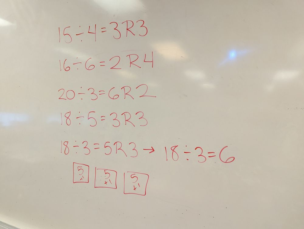 Division equations written on a white board. All of the equations include a remainder.