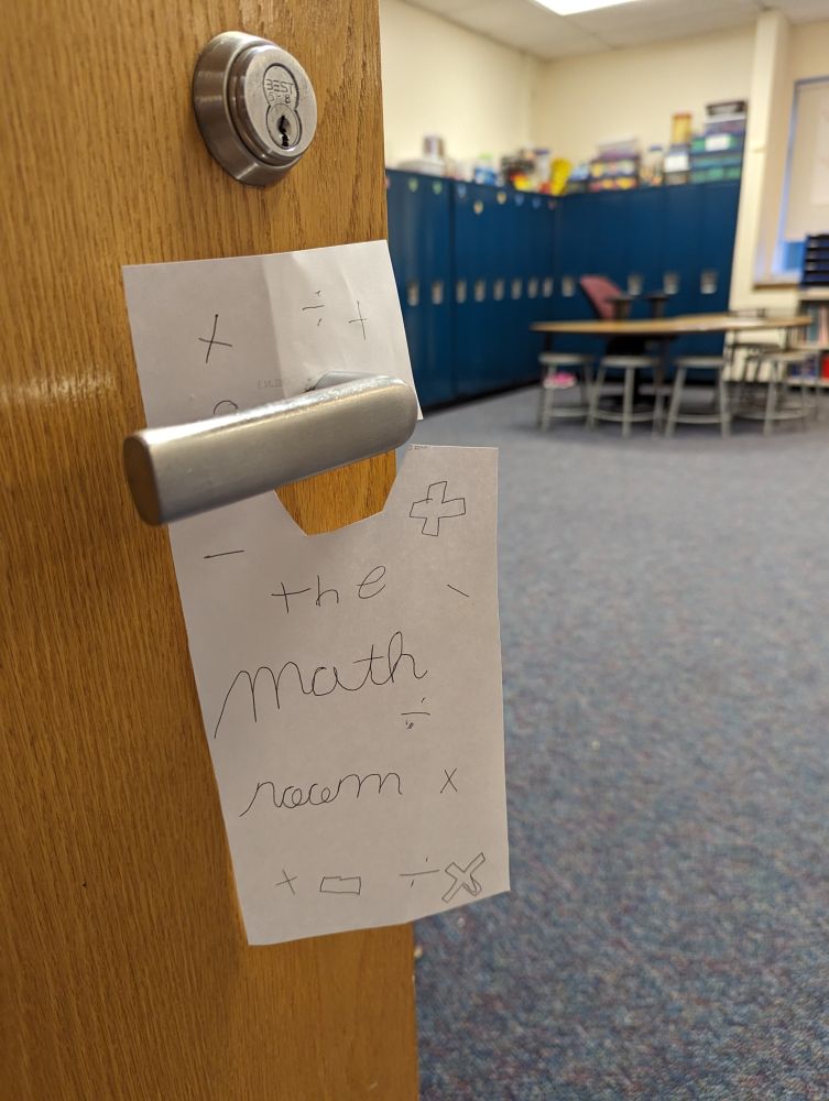 Close up of a door handle with a paper hangar that says "The Math Room"