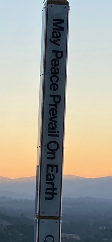 Sunset behind a pole that says “may peace prevail on earth”
