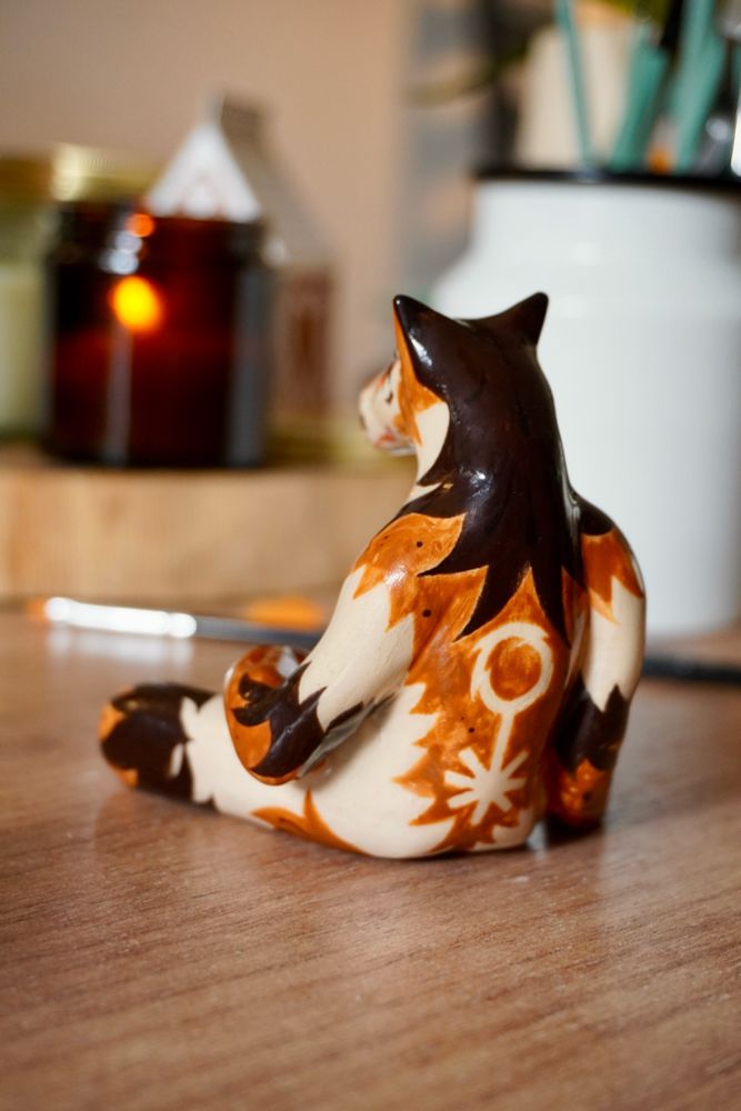 Ceramic sculpture of a werewolf with top surgery scars, seen from the back. They have long mullet and queer sign on their back.