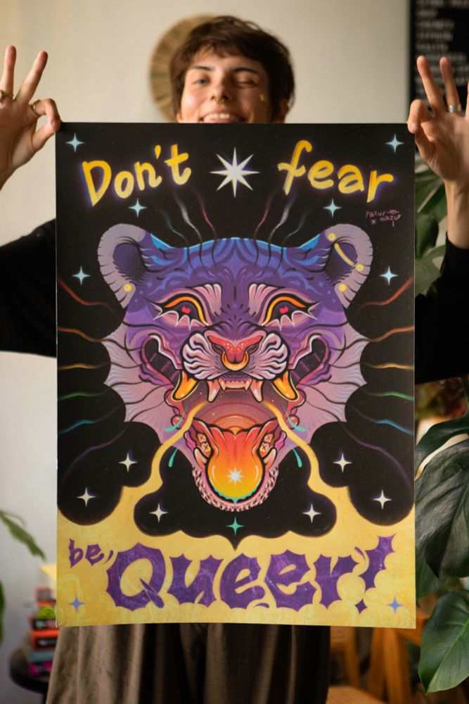 Person holding poster with a purple tiger head in the middle. Yellow mist is coming out of its mouth and there are stars and rainbow whiskers around it. The poster says ‘Don’t fear be queer!’