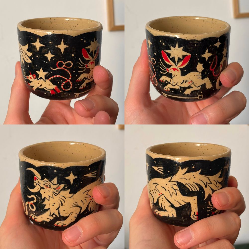 Ceramic cup showed from 4 sides. It shows a parade of animals on a black background with some accents are in red. Mouse, hare, serpent and wolf, holding stars and a moon.