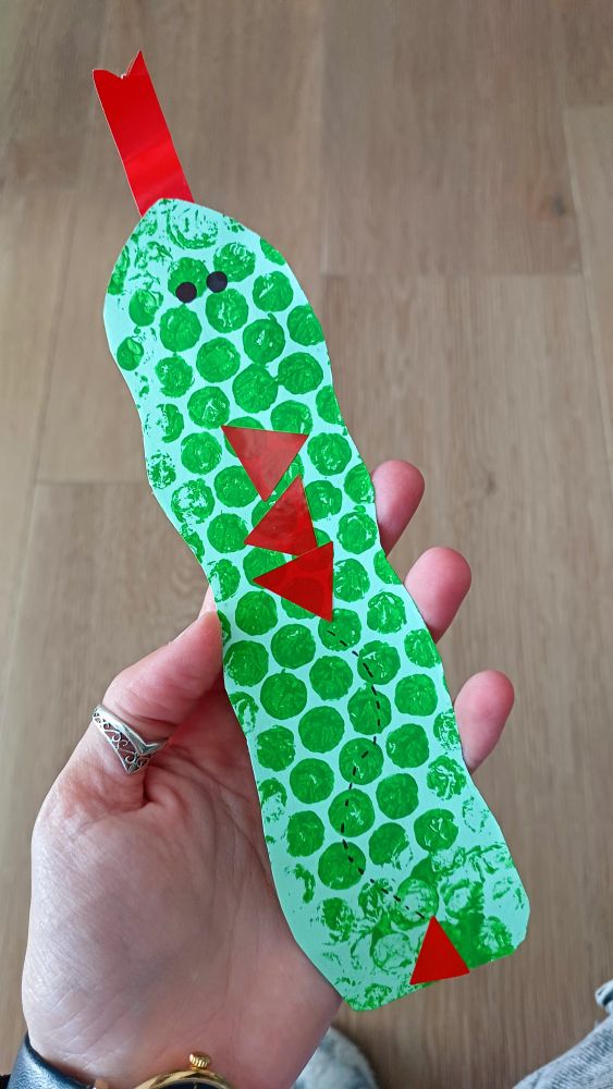 Marcapáginas artesanal hecho de cartulina verde que simula una serpiente. Tiene una especie de lazo arriba que simula la lengua y puntitos verdes pintados con pintura de dedos que simulan las escamas. 