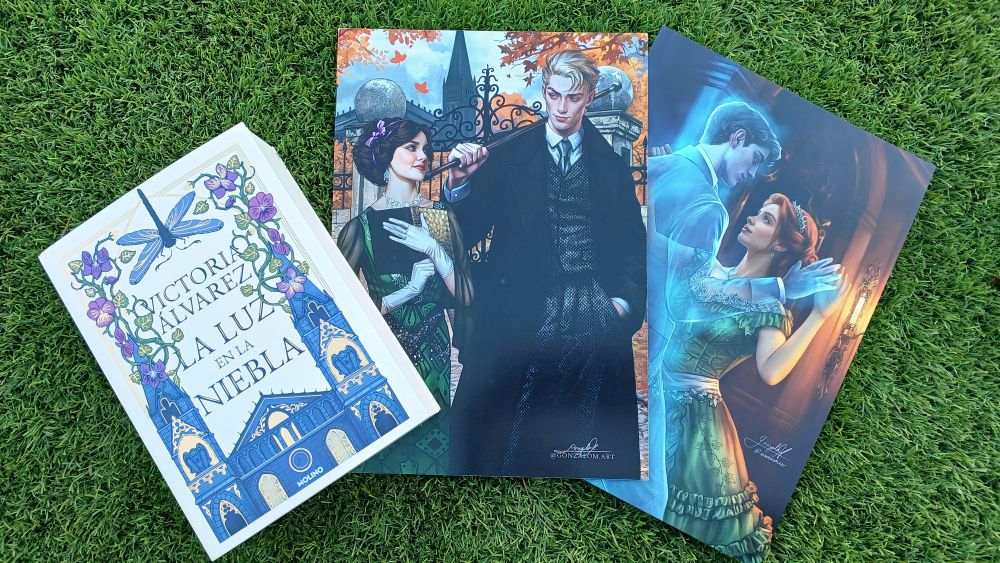 El libro junto a dos prints de tamaño A4 con escenas de los libros La luz en la niebla y Hojas de dedalera. 