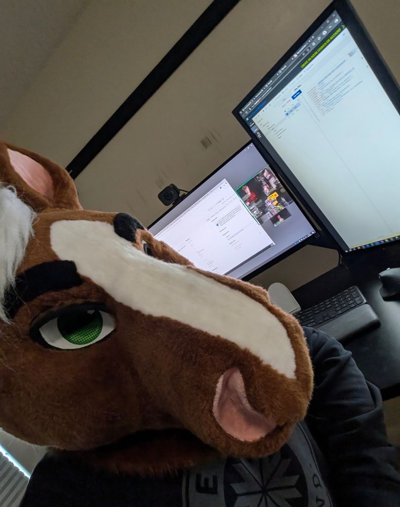 Horse fursuiter with two computer monitors behind him showing a Zoom meeting. Attendees blurred out 