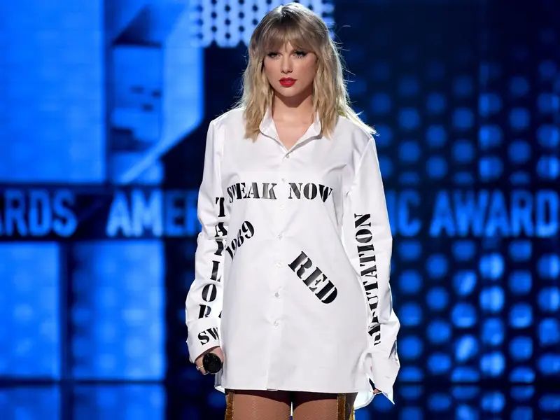 Taylor Swift at the AMAs wearing a white shirt with her first six album titles written in black 