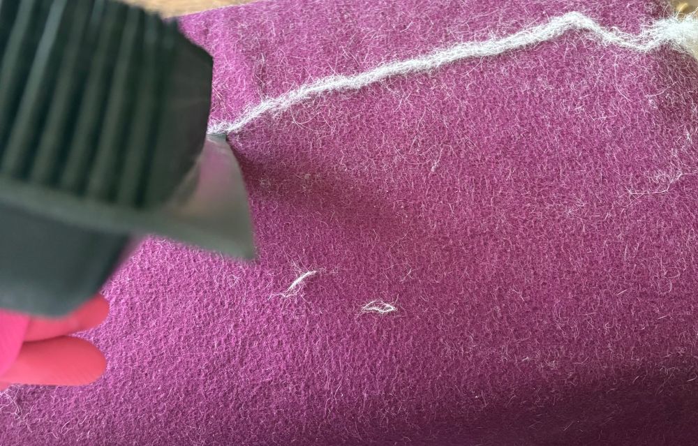 Purple fleece blanket with a line of white cat cat fur that’s been partially scraped off. Rubber broom with scraper on left of photo.