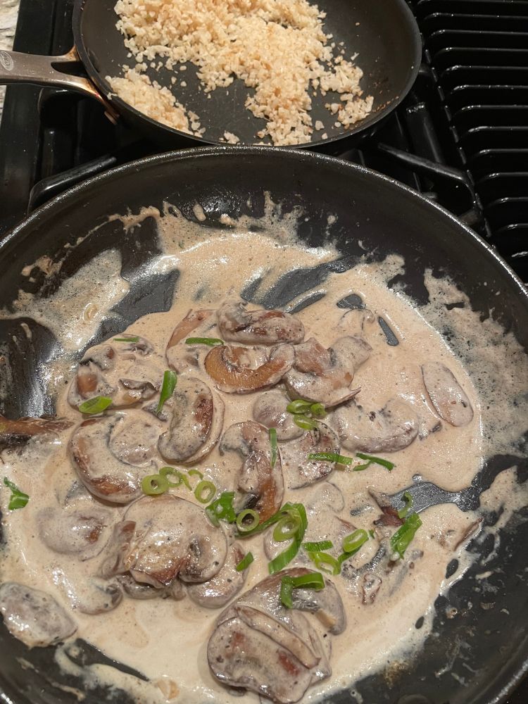 2 skillets, one with toasted riced cauliflower and one with a mushroom cream gravy with green scallion garnish.