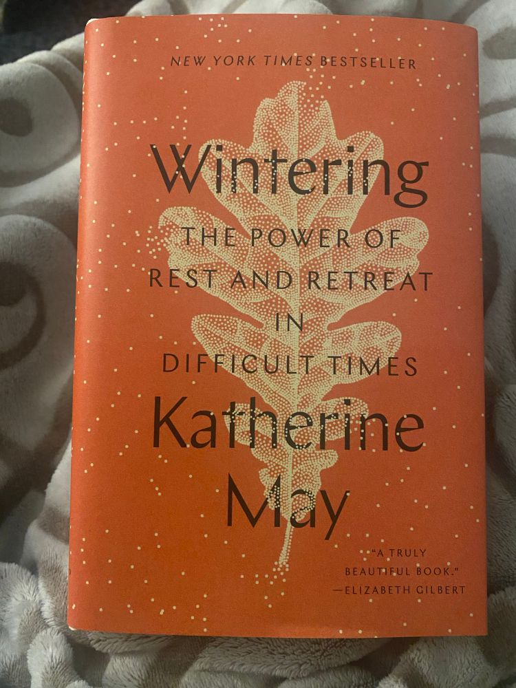 Book cover for Wintering: The power of rest and retreat in difficult times by Katherine May. Burnt orange background with a light orange leaf created with small dots and surrounded by small dots representing snow.