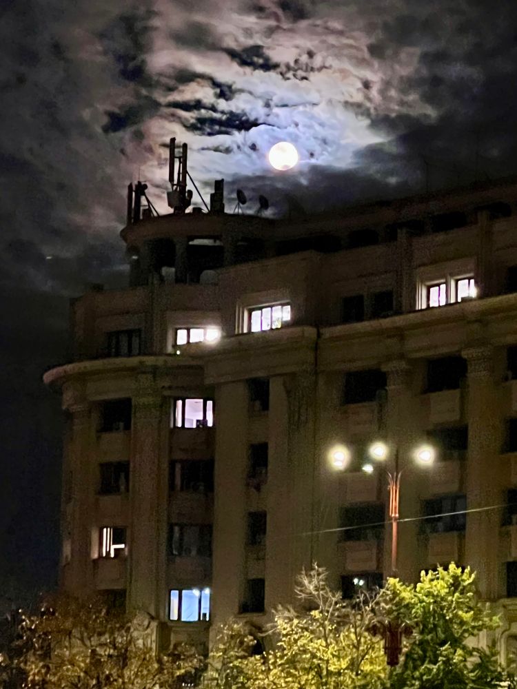 Ein Altbau. Darüber strahlt der Vollmond am bewölkten Nachthimmel 