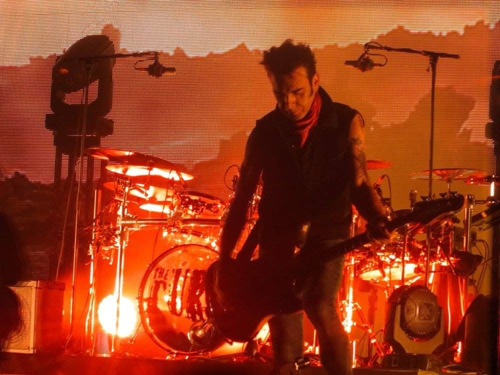 The Cure bassist Simon Gallup on stage under red lighting 