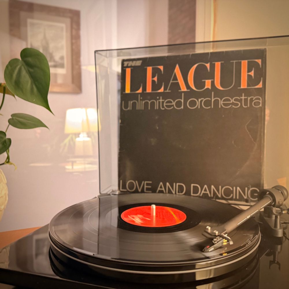 A copy of The League Unlimited Orchestra’s album Love and Dancing spinning on a turntable with the album cover propped up behind. 