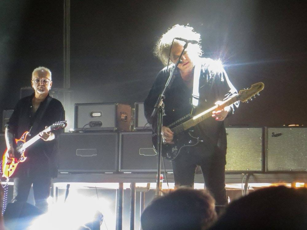 Robert Smith and Reeves Gabriels of The Cure each playing guitar on stage. 