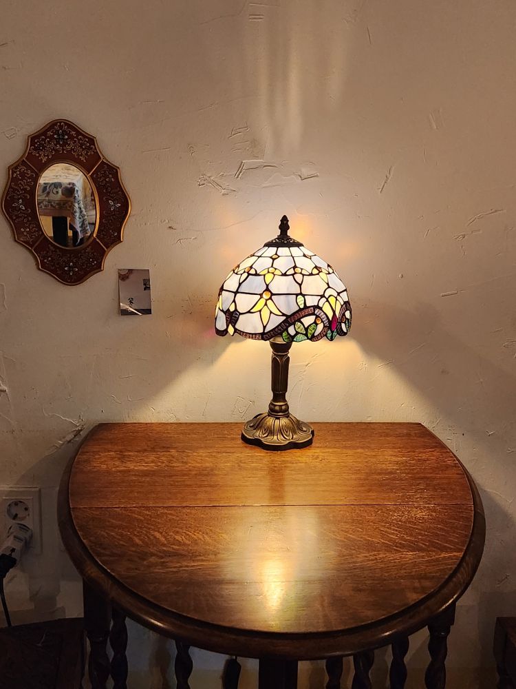 원의 모퉁이를 자른 모양의 작은 테이블. 그 위에 스테인글라스 갓을 씌운 스탠드가 있다.