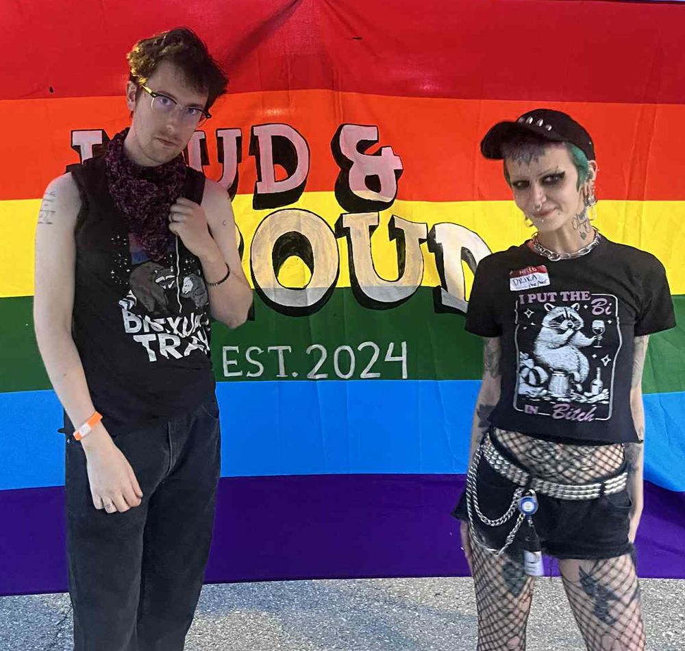 J. Trafford and Candrika Rice posing in front of raindbow Loud & Proud Est. 2024 flag.