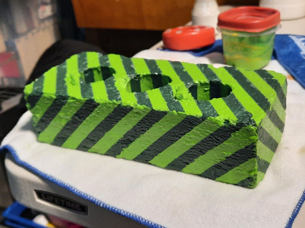 A standard brick painted with dark and light green stripes 