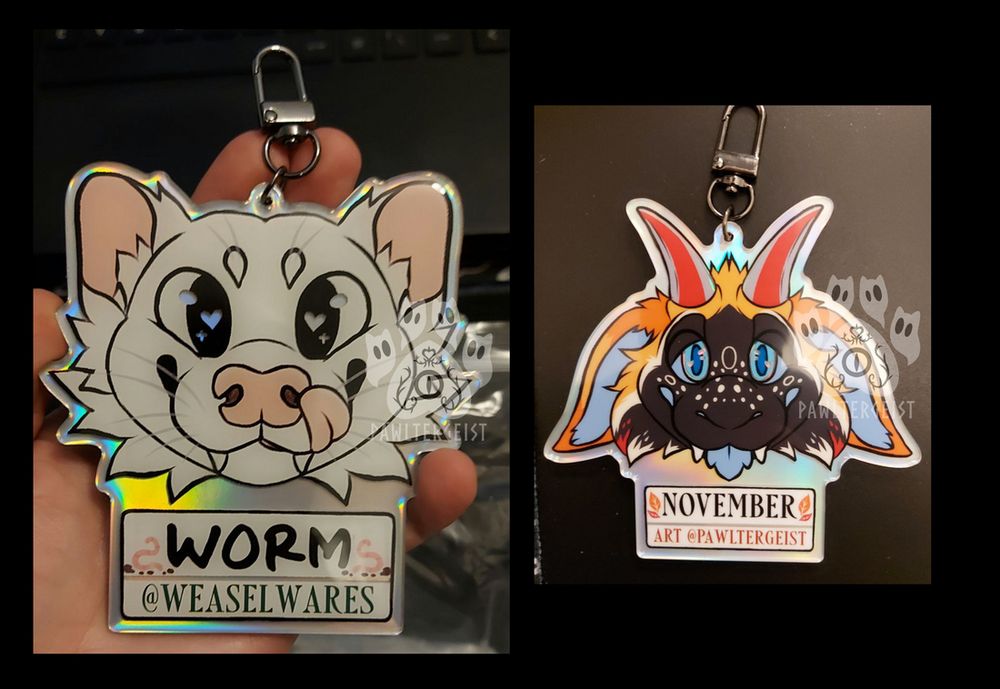 Acrylic badges of two different characters - the left one is a white weasel. The right one is a black, orange and blue alladon with red and grey horns.