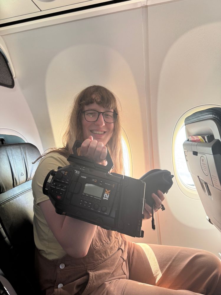 Picture of me holding up my black magic Ursa Mini Pro 12K camera, with the shot clearly taken from inside an airplane 