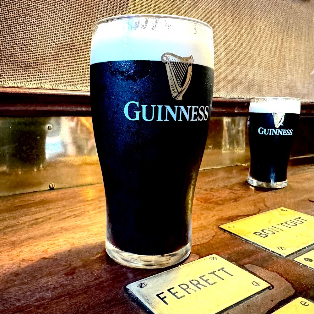 a beautiful pint of Guinness next to a brass stamp that says ferrett and a half pint in the background